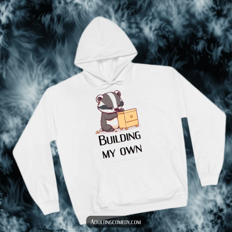Funny badger hoodie showing a busy animal carefully assembling wobbly furniture, a cozy funny gift.